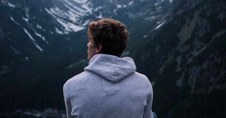 Solo Travelers - A Man in White Hoodie Sitting on a Rock Across the Mountains