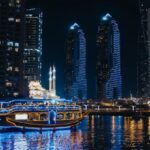 Night Sailing - A Boat Sailing on River Near City Buildings during Night