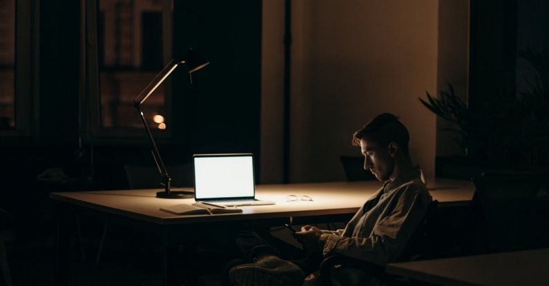 Overnight Stay - Man in Black and White Stripe Dress Shirt Sitting on Chair in Front of Macbook