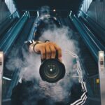 Photography - Man Holding Camera While Squating With Smoke on Face Inside Building