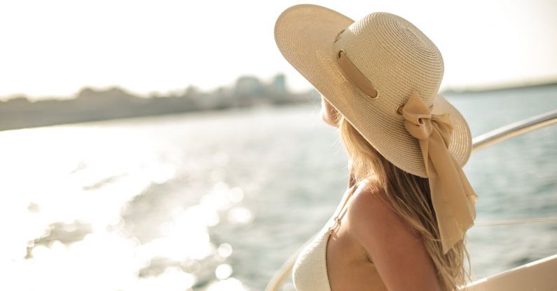 Luxury Cruise - Back view of slim female in bikini top and straw hat enjoying trip on cruise boat on sunny day while relaxing during summer vacation and looking away