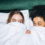 Best Time - Two Young Women Lying on White Bed While Looking at Each Other