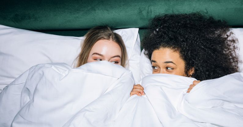 Best Time - Two Young Women Lying on White Bed While Looking at Each Other